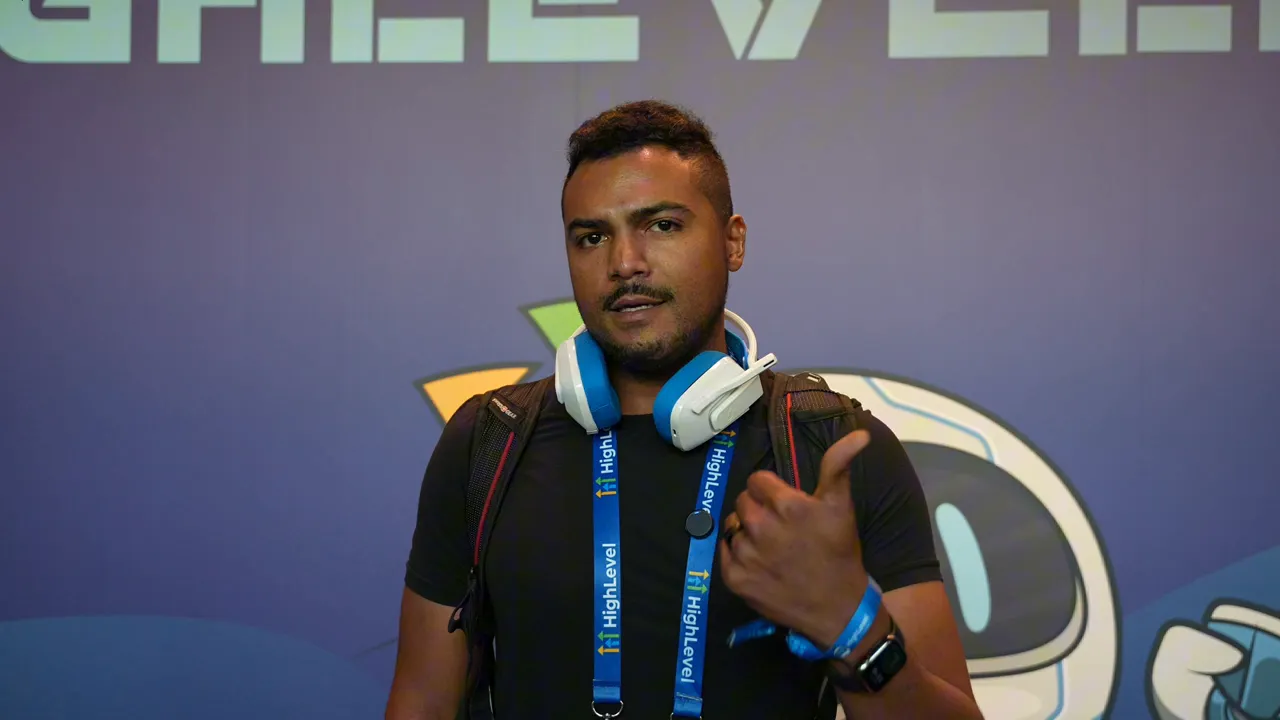 Speaker with headphones and conference lanyard standing centered in front of a GFunnel/HighLevel branded wall