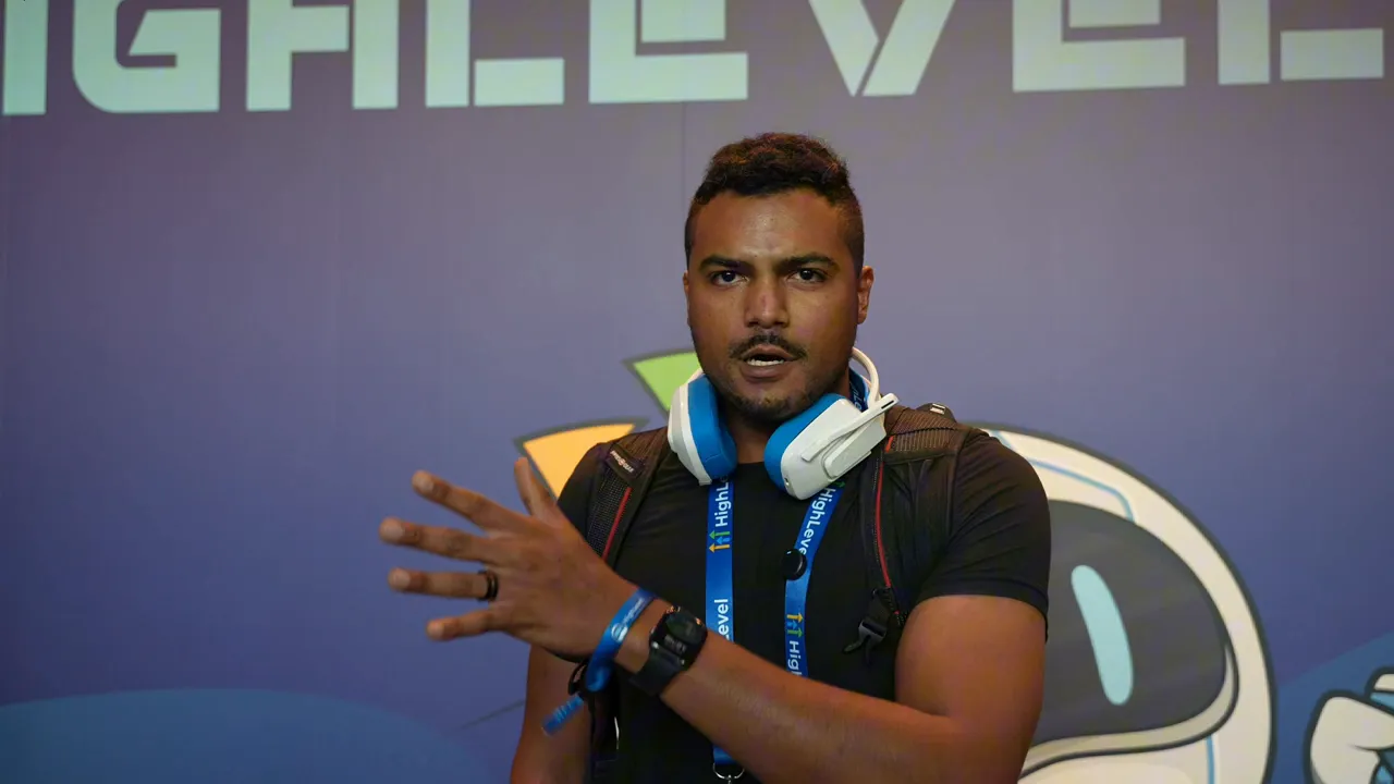 Conference speaker gesturing with hand while wearing headphones and a lanyard against a purple GFunnel-branded backdrop