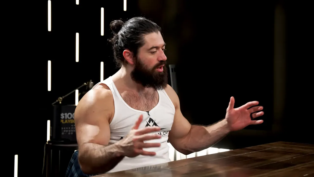 Presenter using wide hand gestures while speaking at a wooden table, studio lights in background