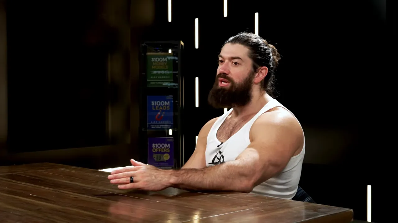 Presenter seated at a wooden table using hand gestures to explain a concept, with marketing resource covers visible on a shelf behind