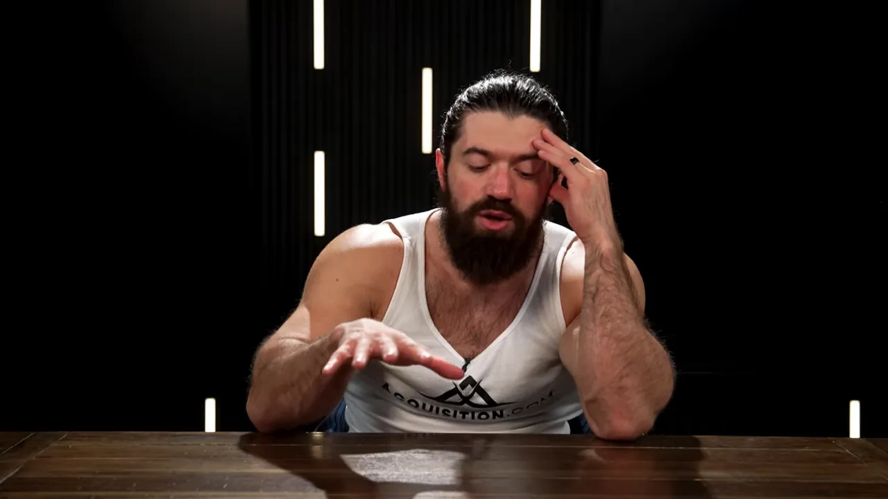 Presenter gesturing with one hand over the table while touching his forehead, explaining a concept