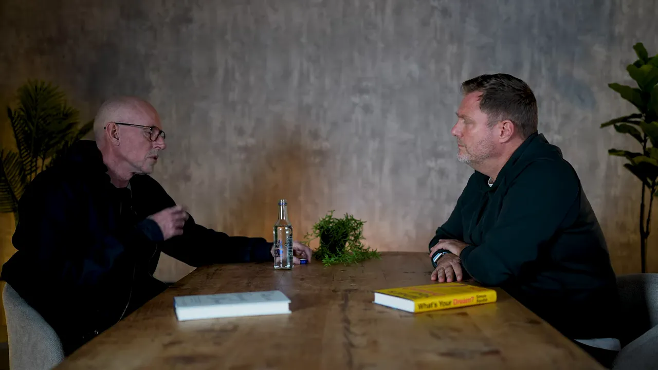 Wide shot of two people across a table with one person gesturing while making a point