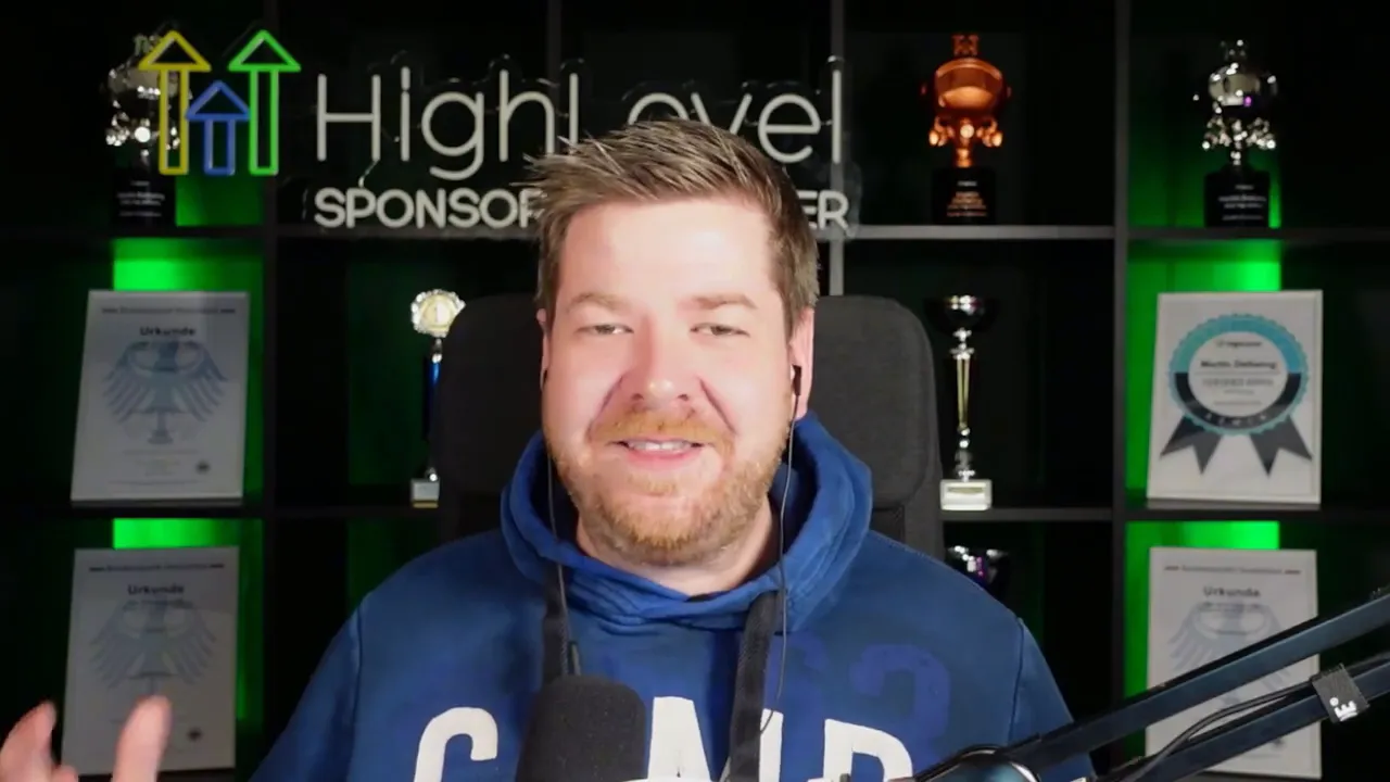 Wider shot of a speaker gesturing in front of a HighLevel-branded backdrop with trophies and certificates, microphone and boom arm visible.