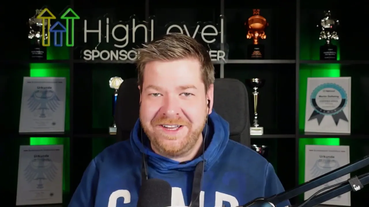 Speaker centered in front of a HighLevel-branded backdrop with trophies and microphone, talking to camera.