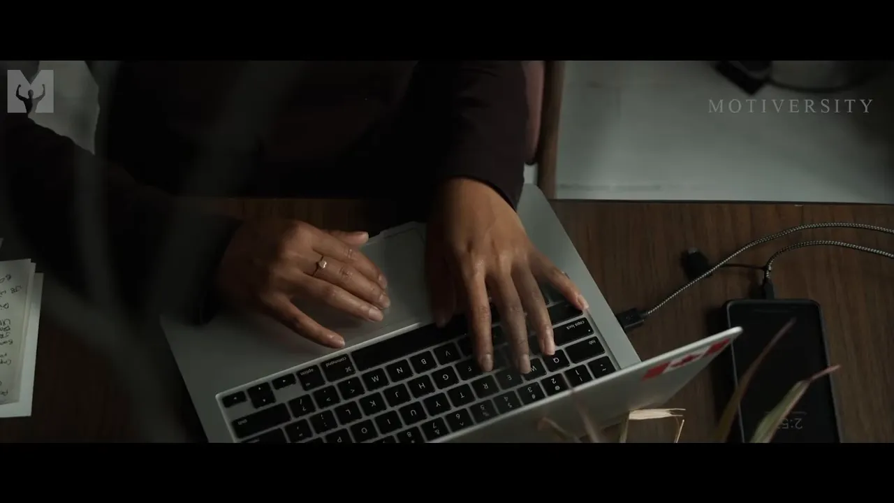 Close-up of hands typing on a laptop keyboard with a smartphone nearby