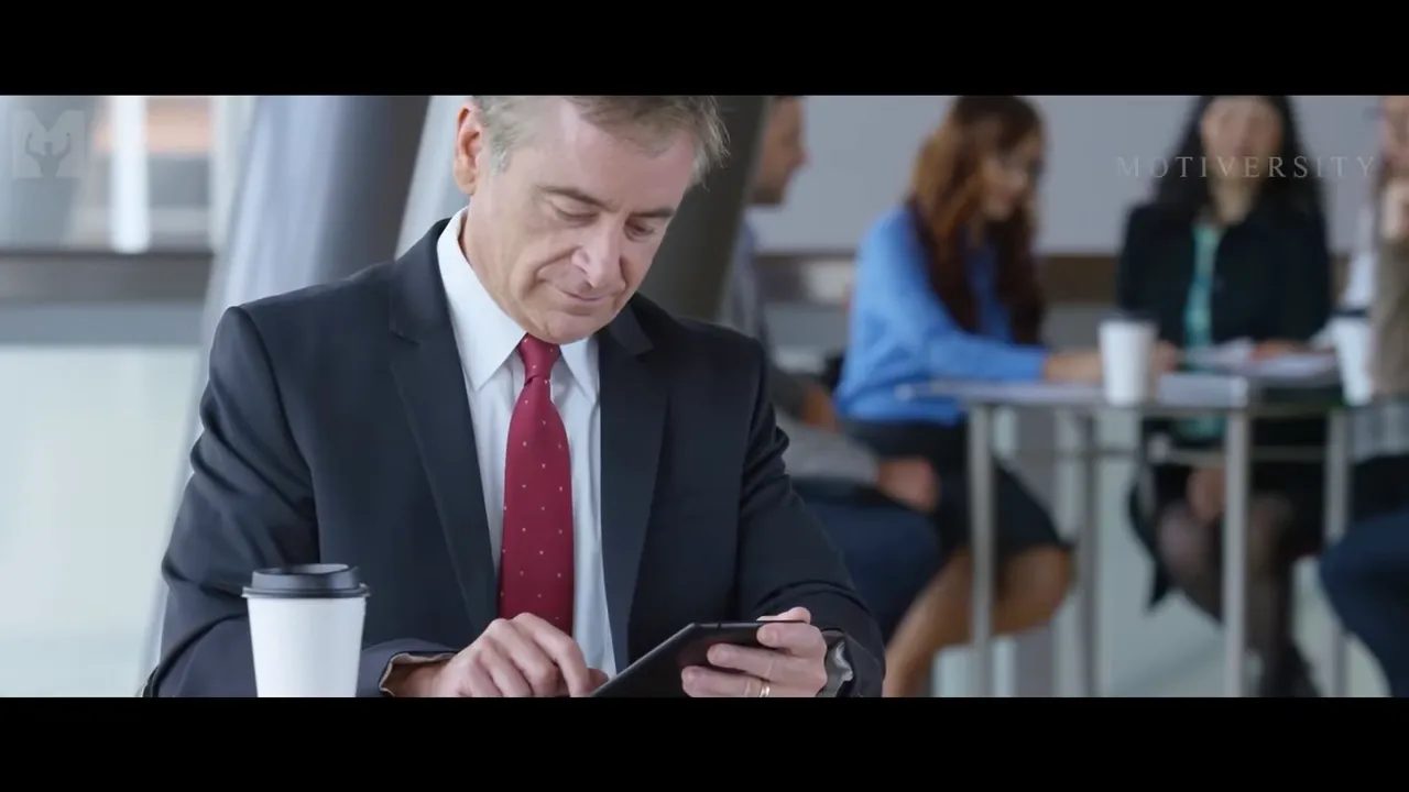 Businessman using a tablet at a café table with staff and customers blurred in the background