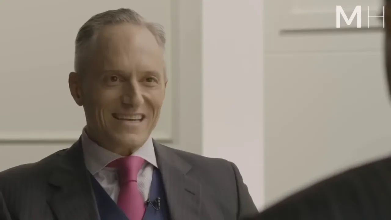 Interview shot of a host smiling and listening while a guest silhouette appears in the foreground