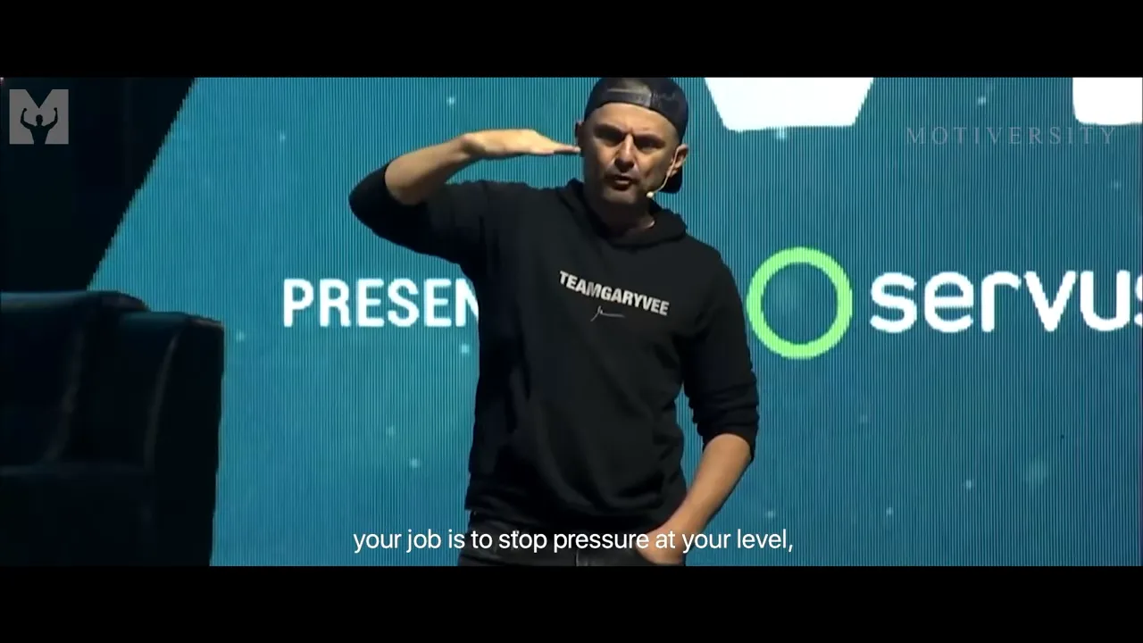 Keynote speaker on stage raising a hand to indicate stopping pressure with subtitle 'your job is to stop pressure at your level,'