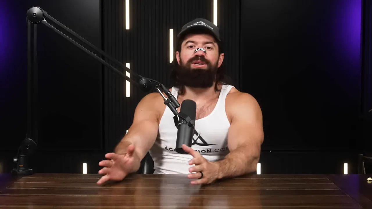 presenter at a studio table speaking into a microphone and gesturing with hands