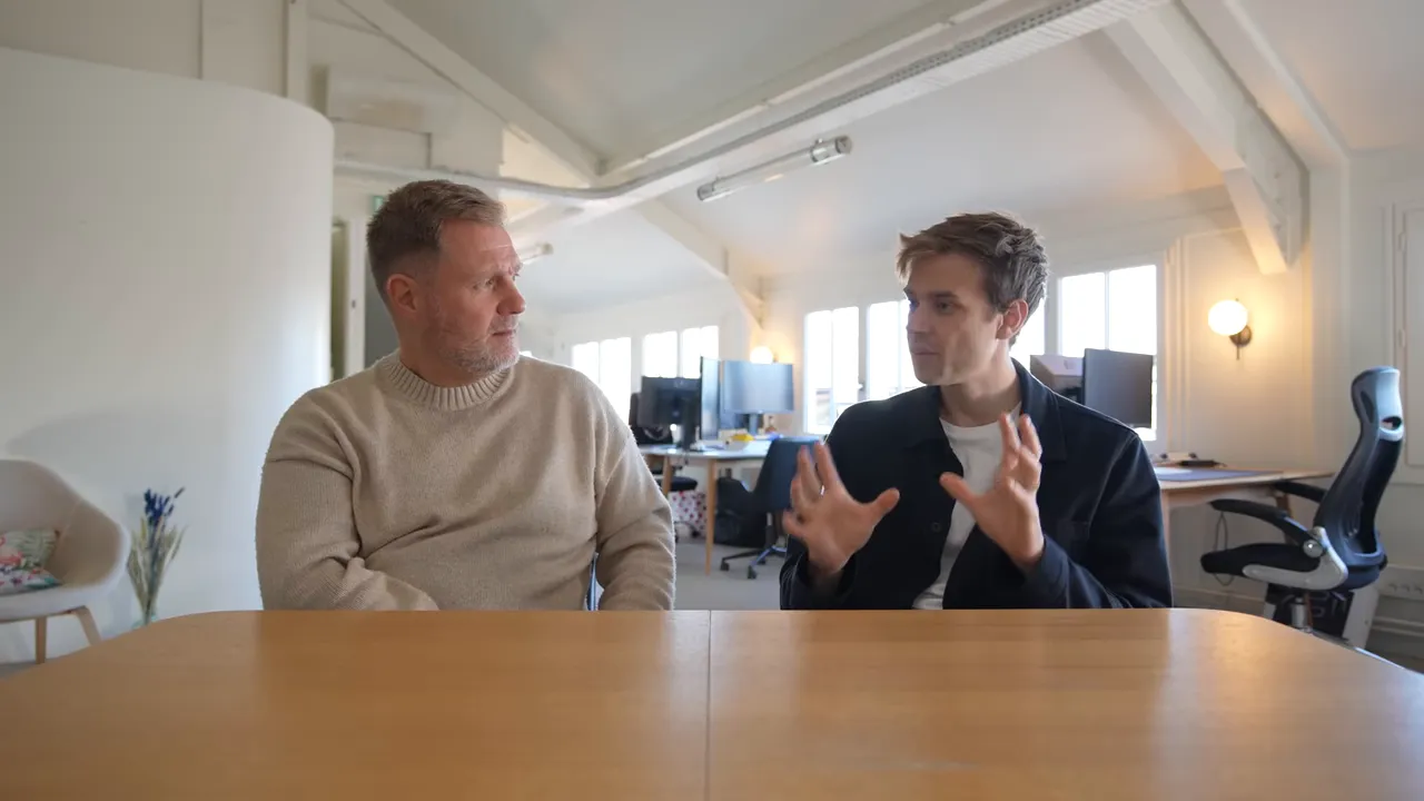 Two people in an office at a table, one actively explaining with hand gestures.