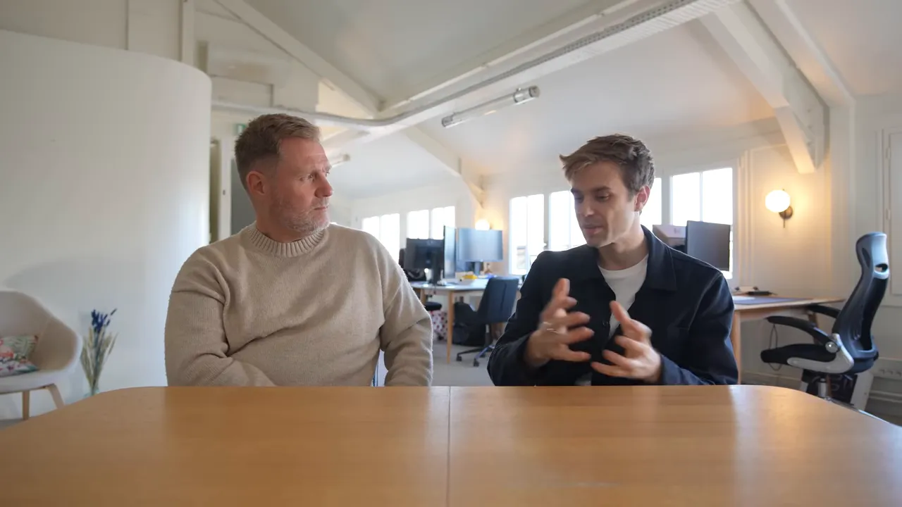 Two founders at a table in an open office gesturing while discussing product and user onboarding