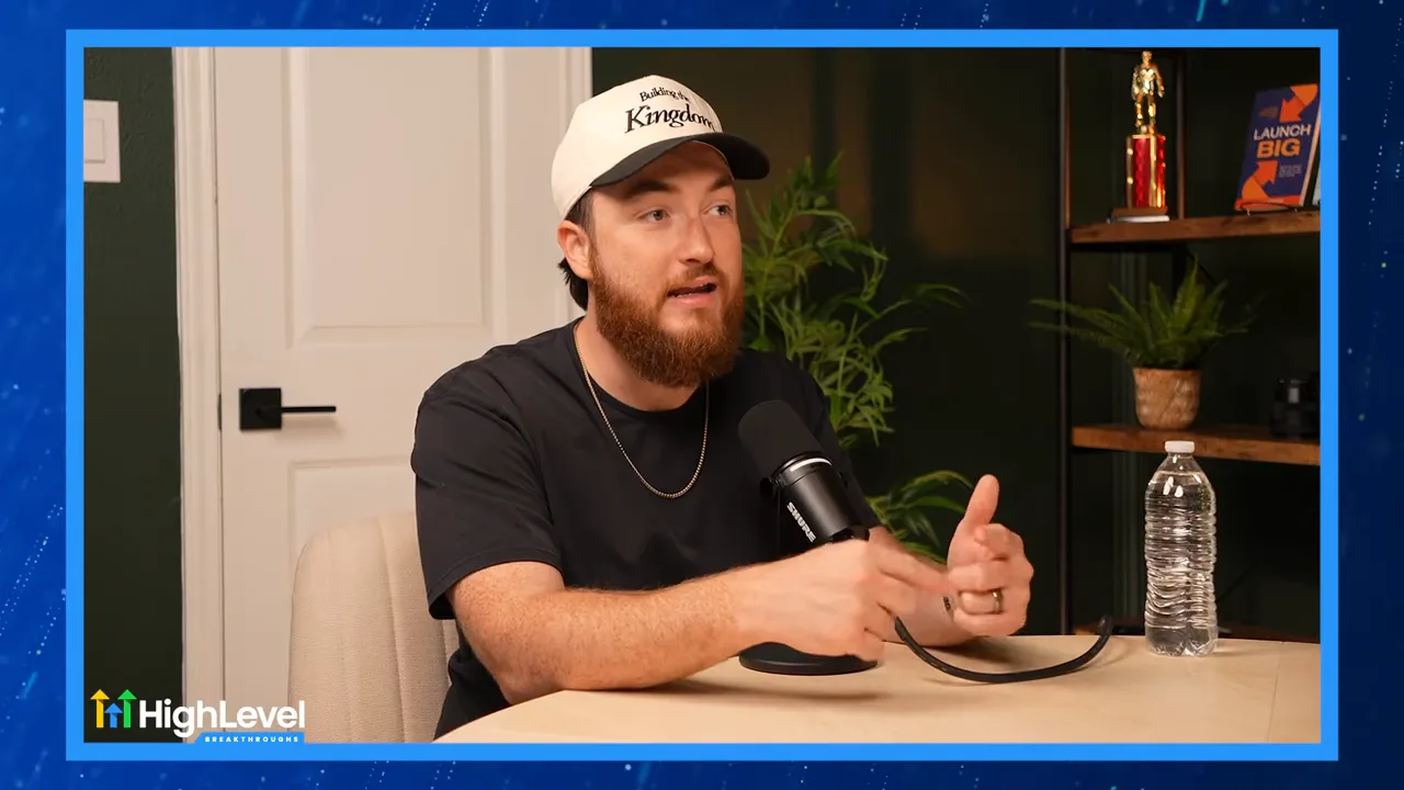 Podcast speaker gesturing while explaining automation, clear microphone visible and studio shelving in the background