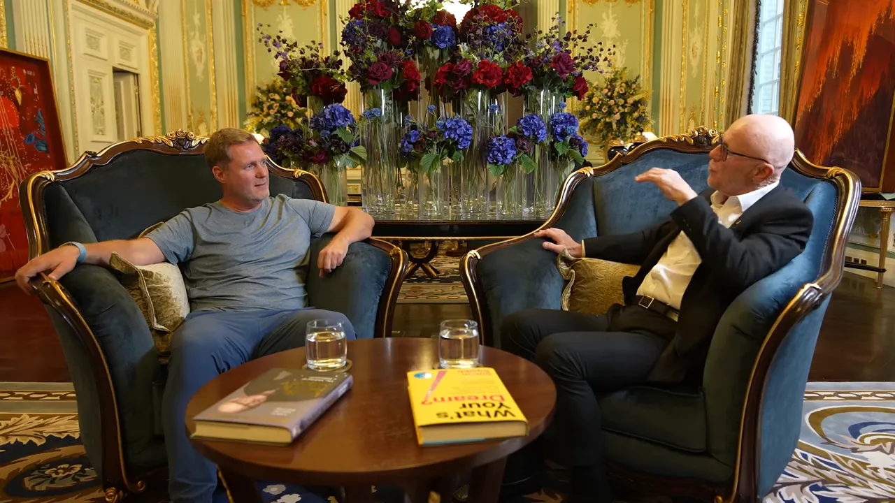 Two people having a face-to-face conversation in armchairs with books and glasses on a table