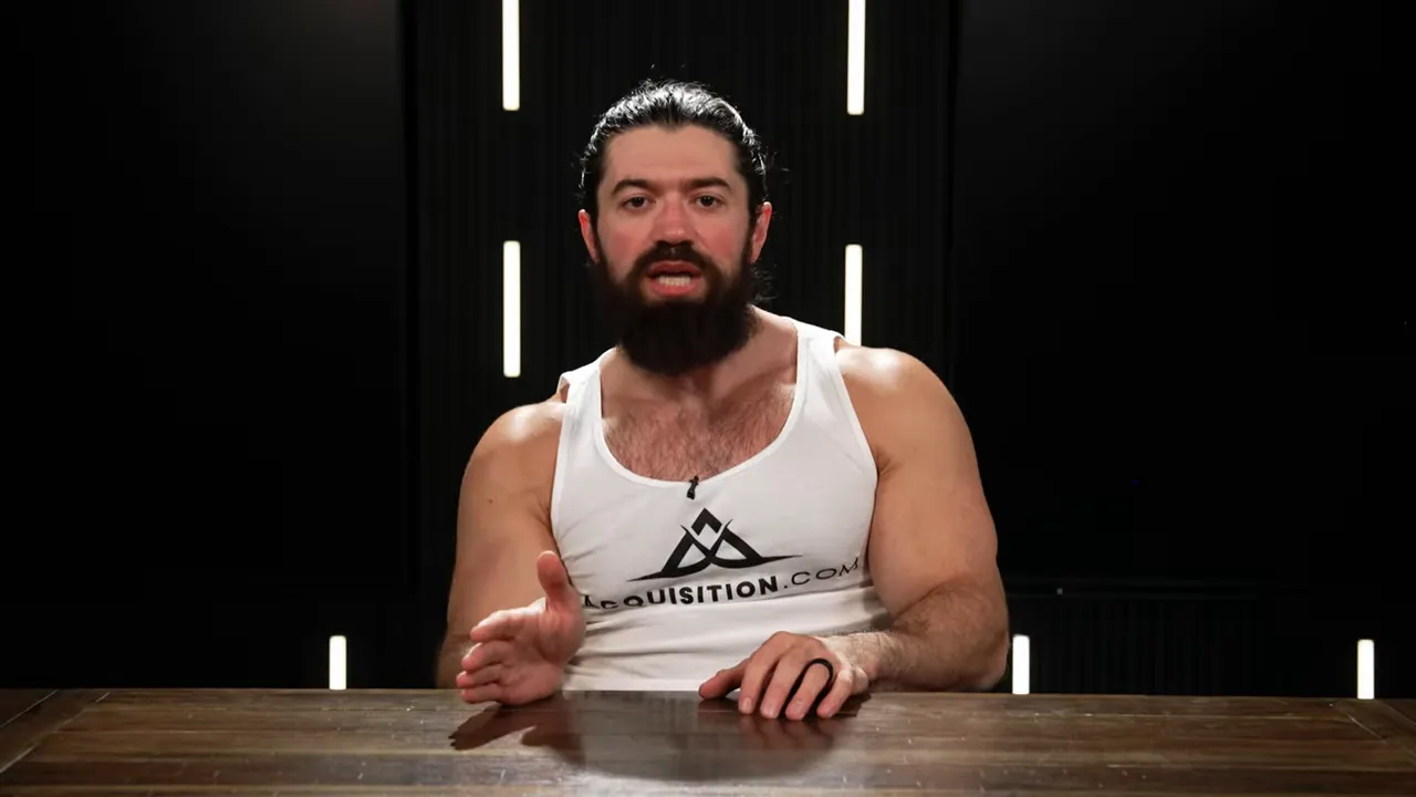 Presenter addressing the camera with one hand extended while explaining a point in a dark studio.