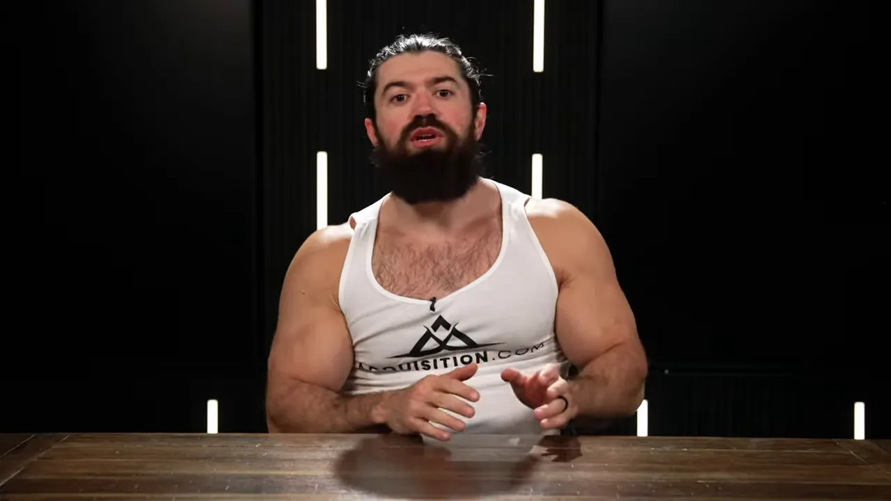 Presenter leaning forward at a table speaking to camera with hands visible, dark studio background with vertical light strips
