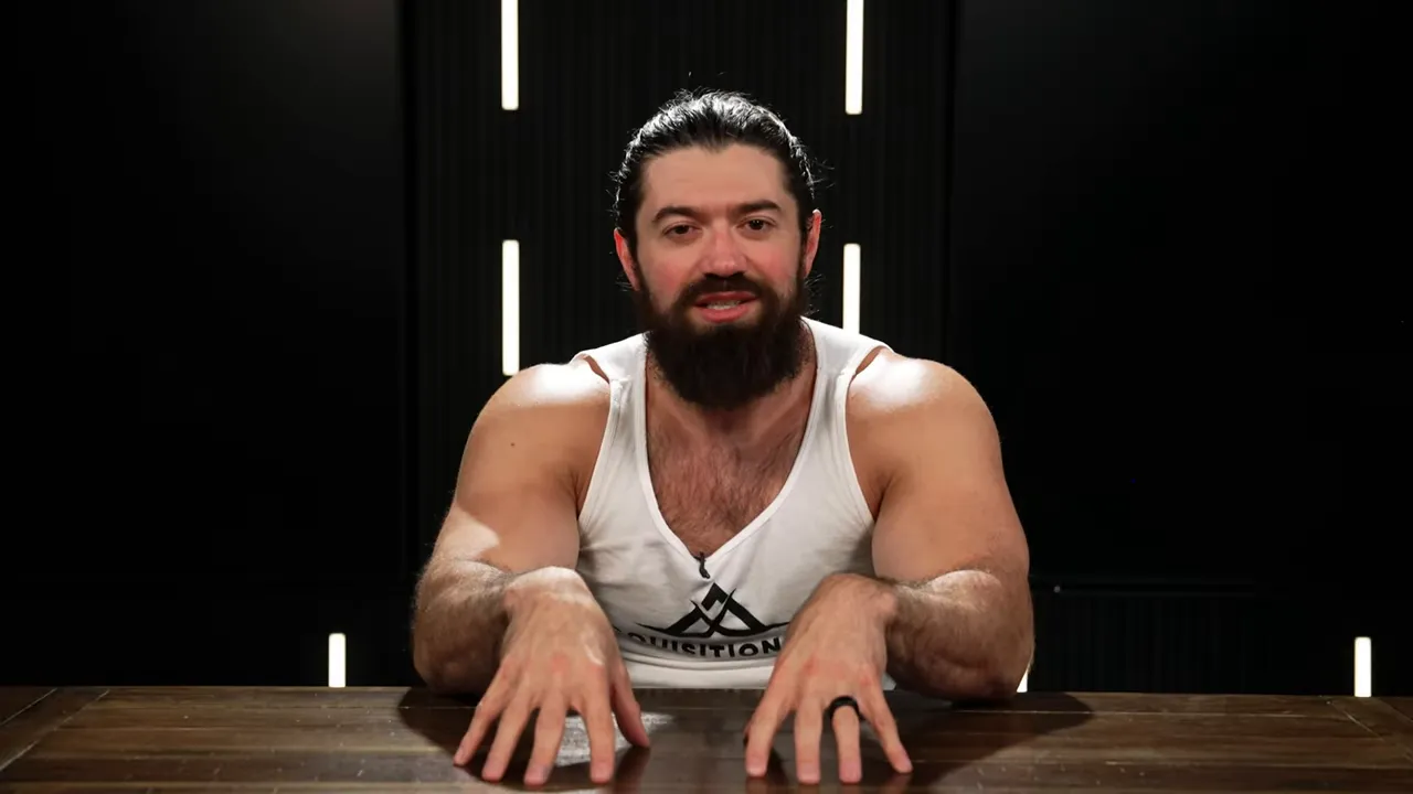 Presenter seated at a desk, smiling slightly with hands on the table, addressing the audience.