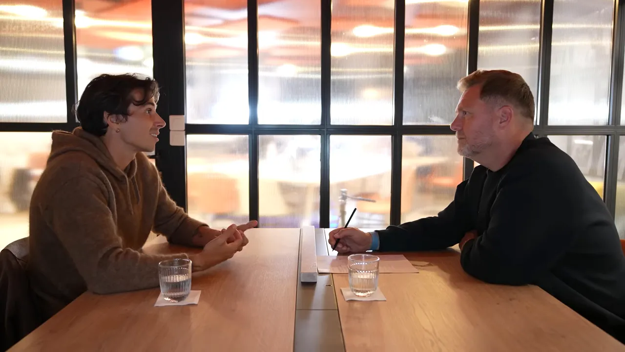 Two people having a discovery-style meeting across a wooden table with glasses, notes, and open gestures.