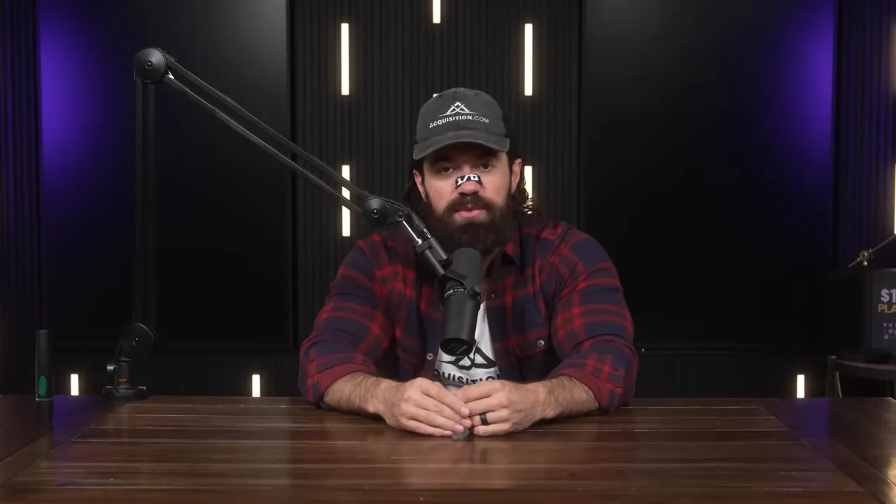 Podcast host sitting centered behind a wooden table, hands clasped, speaking into a microphone in a studio