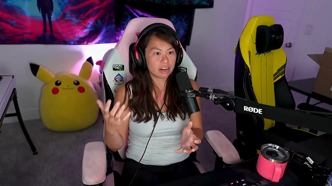 Creator at desk using open hand gestures while talking into a RØDE microphone, visible streaming setup and Pikachu plush