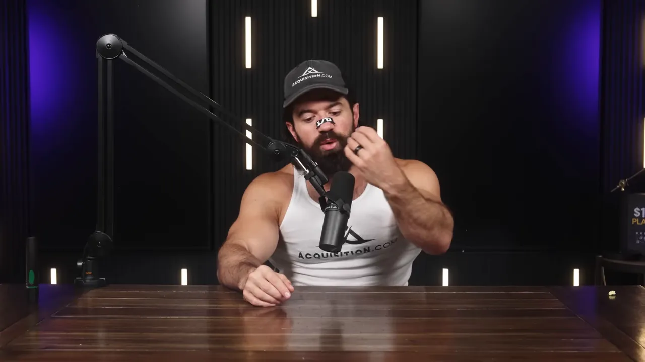 Podcast host leaning forward and examining his hand while speaking into a microphone with studio lighting and dark acoustic panels