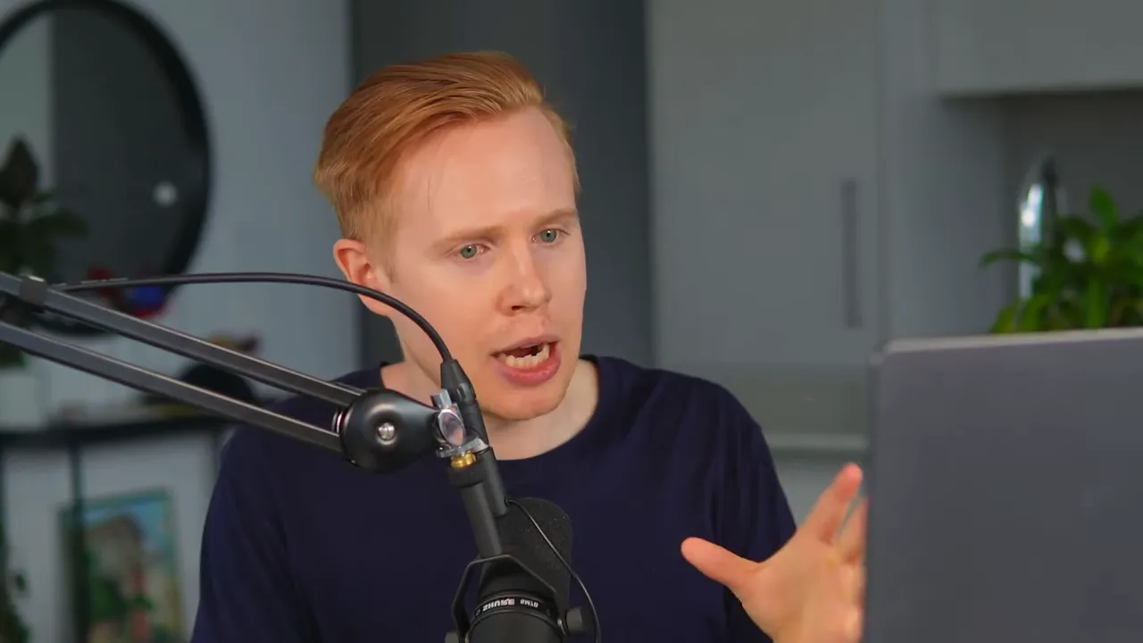 Presenter speaking energetically with a hand gesture, boom microphone and laptop visible