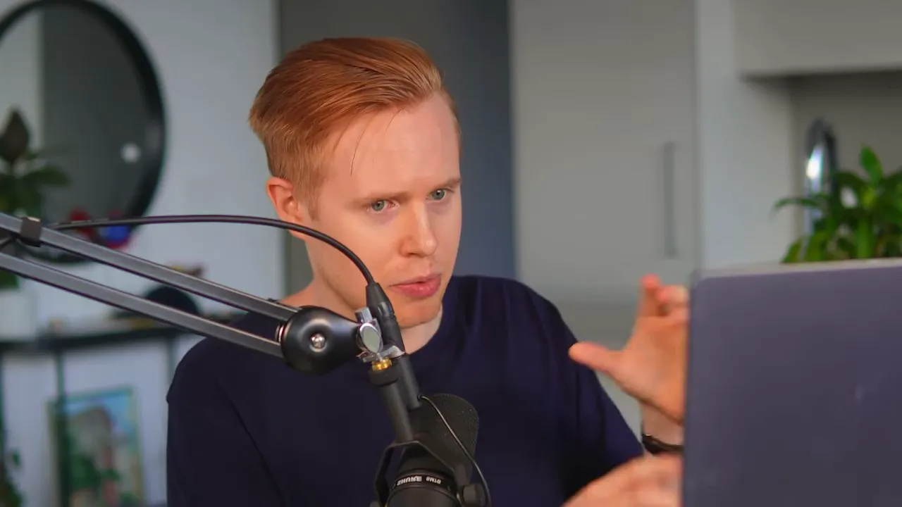 Presenter gesturing with hands in front of a laptop and microphone, visually explaining an automation flow.
