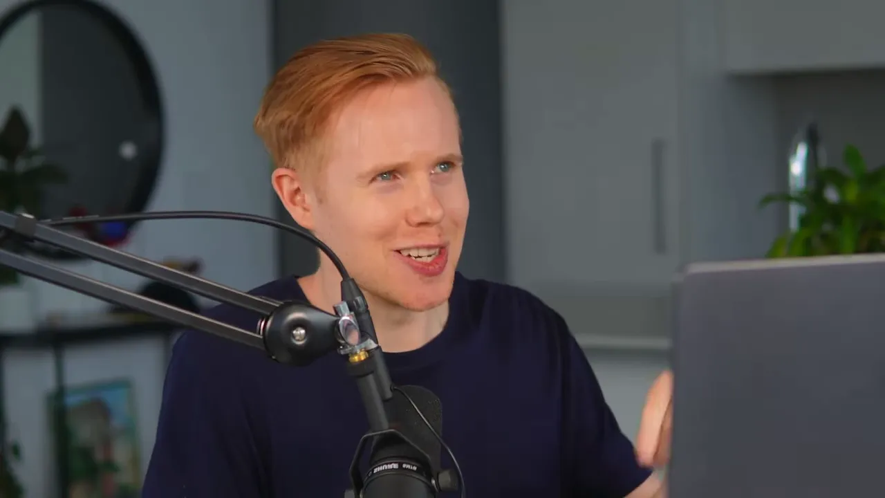 Presenter smiling and gesturing toward a laptop while speaking into a microphone