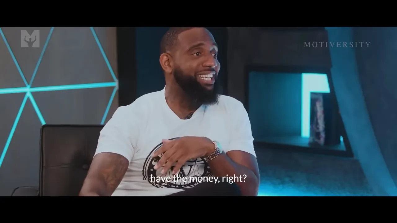 Interview shot of a man smiling and gesturing with the subtitle 'have the money, right?'