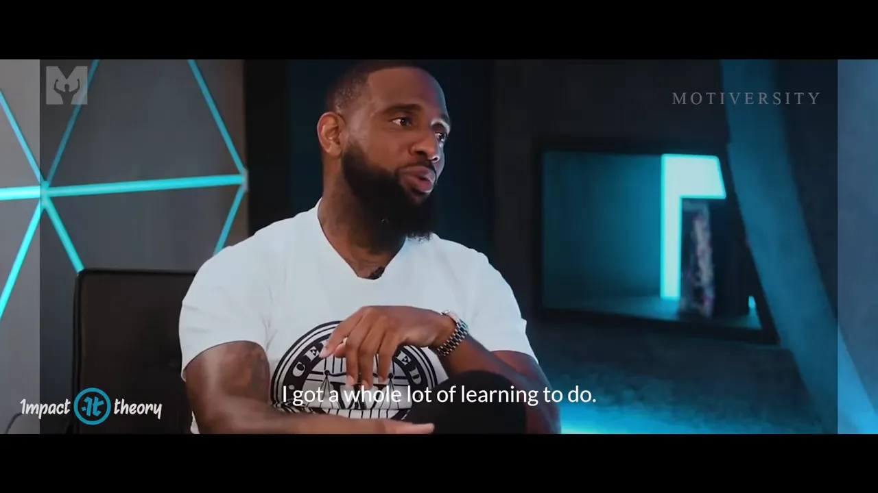 Studio interview speaker mid-answer in a blue-lit set, hands folded and subtitle 'I got a whole lot of learning to do.'
