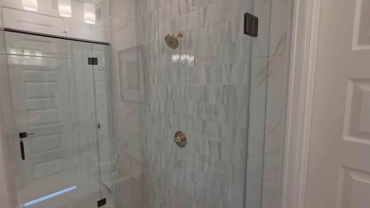 Modern spa-style shower with textured wall tile, gold-tone shower fixtures and frameless glass door