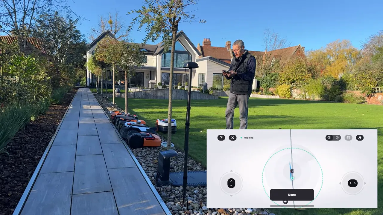 Person holding a phone beside the Navimow RTK mast with the app mapping interface visible and the mower staged nearby