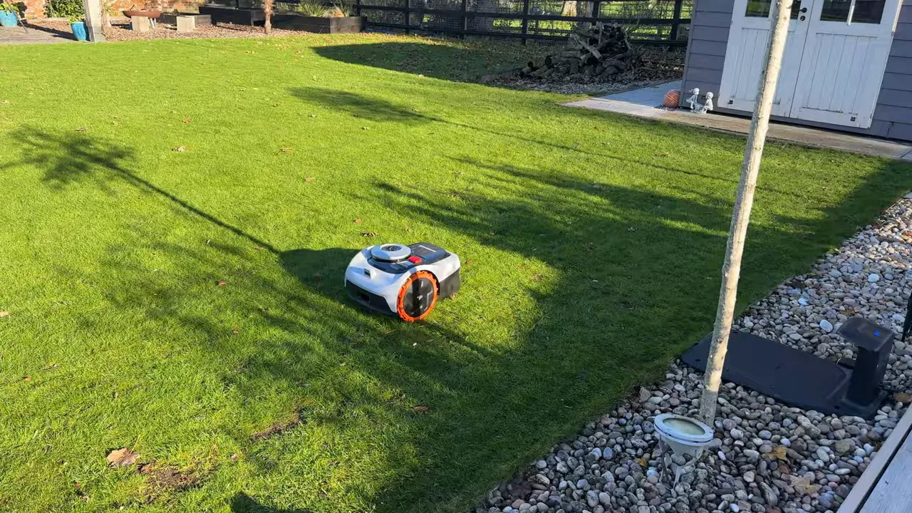 Navimow i105 robotic mower cutting grass on a suburban lawn with pebble border and RTK dock visible at the edge
