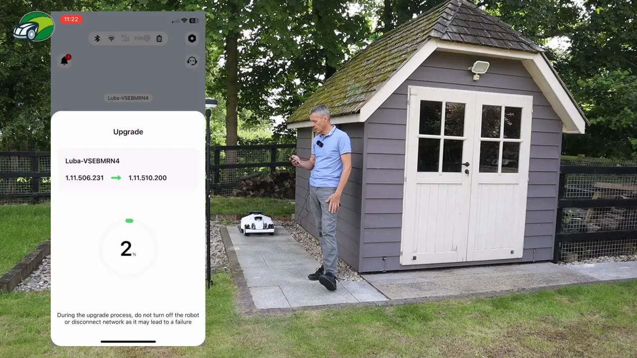 Mammotion app upgrade screen showing 2% progress and the Luba 2 on its charging base beside a garden shed.