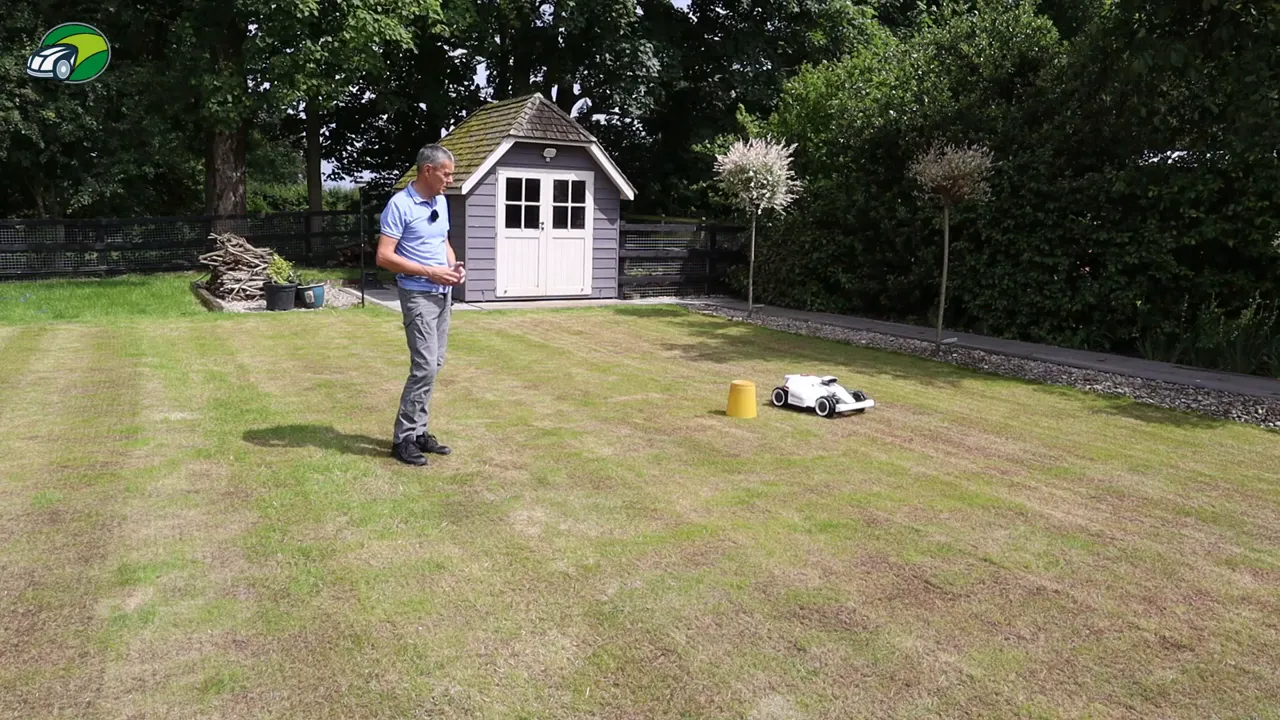 Luba 2 robotic mower navigating around a yellow bucket obstacle during avoidance testing with presenter nearby