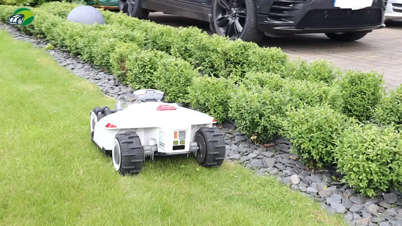 Rear view of Luba 2 robotic mower close to a hedge and gravel strip, showing wheels and deck alignment
