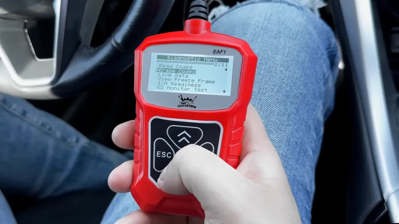 Handheld red OBD2 code reader showing diagnostic menu in a car interior
