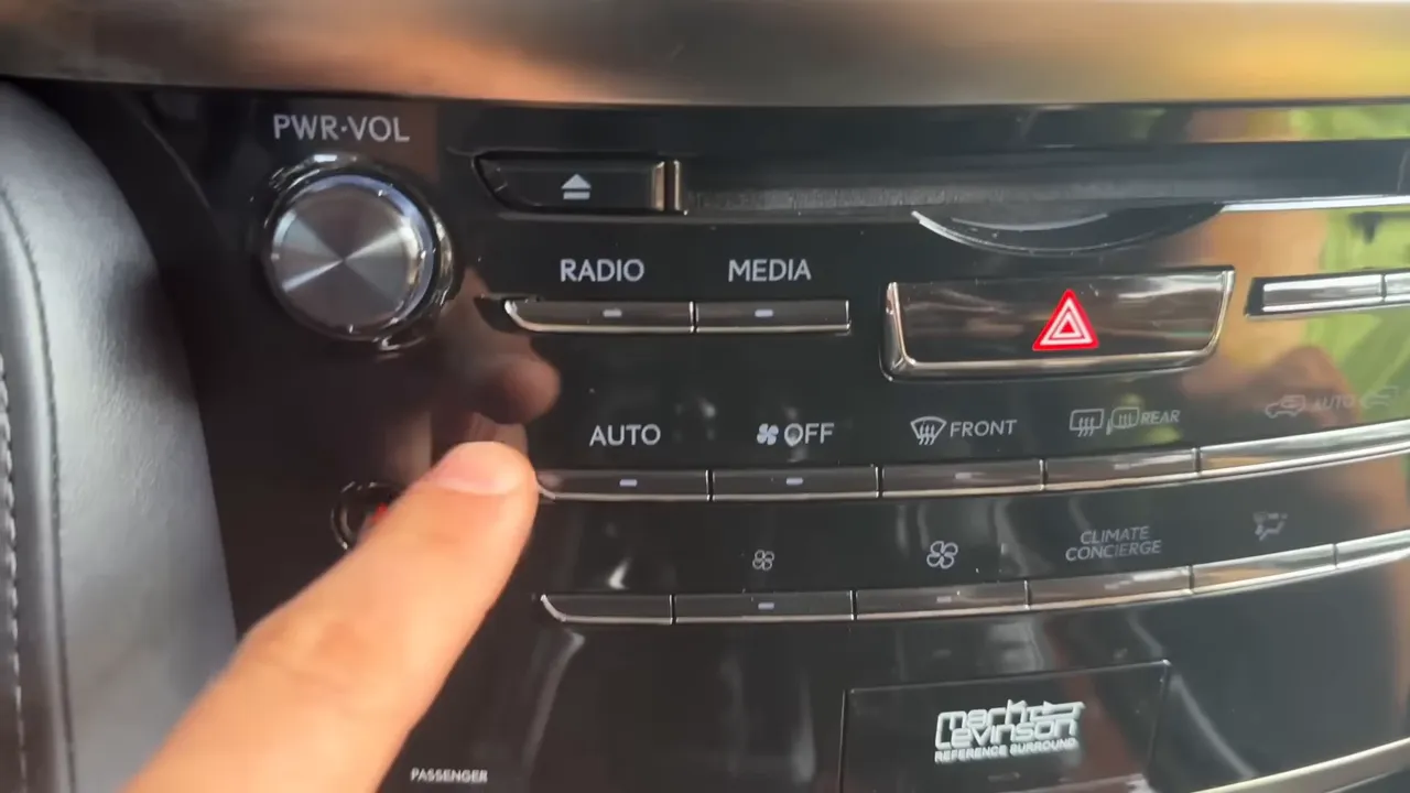 Finger pressing a car climate control button on the center console showing AUTO, radio and hazard buttons