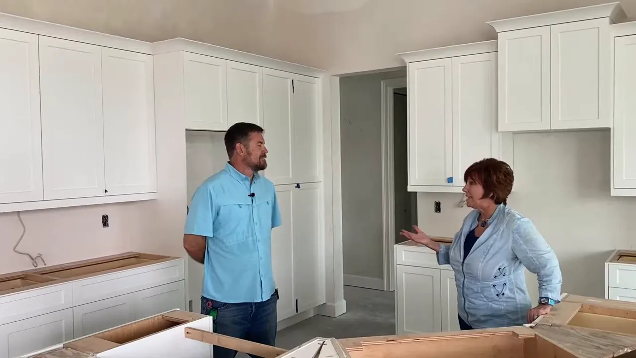 Two people in a mid‑construction kitchen discussing finishes with white cabinetry and island framing.