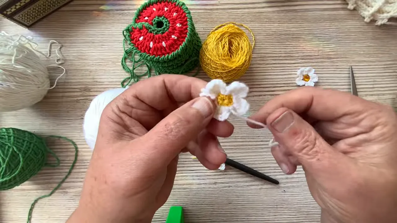 Hands holding a five-petaled white crochet flower with a yellow center