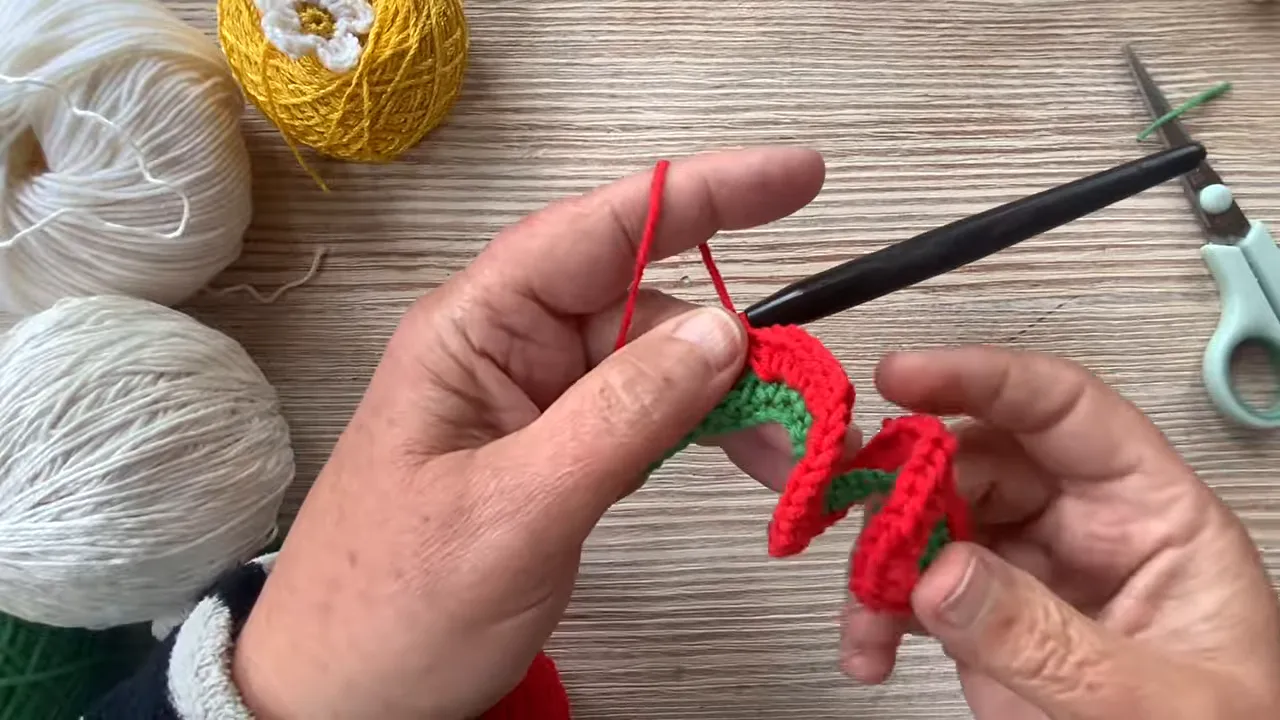 Hands holding a curling red crochet row attached to a narrow green foundation