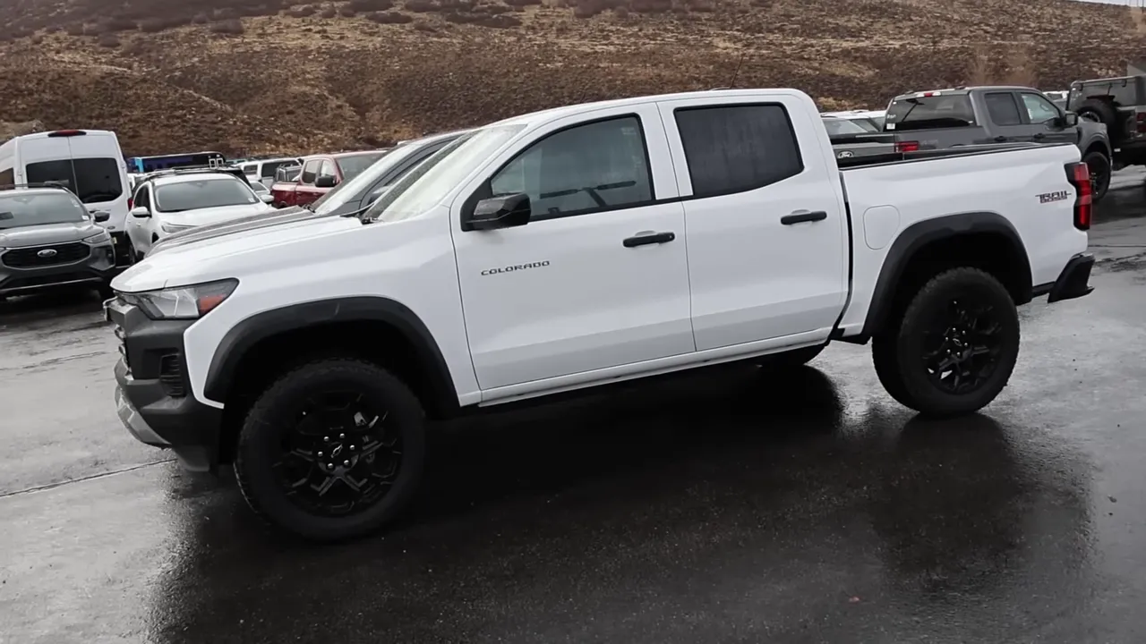 Full side profile of a white Chevrolet Colorado Trail Boss parked on wet pavement, clear view of wheel, fender flares and bed.