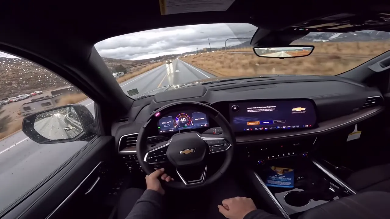 High clarity driver interior view of a Chevrolet Suburban showing steering wheel, digital instrument cluster and wide infotainment screen with clear forward road view