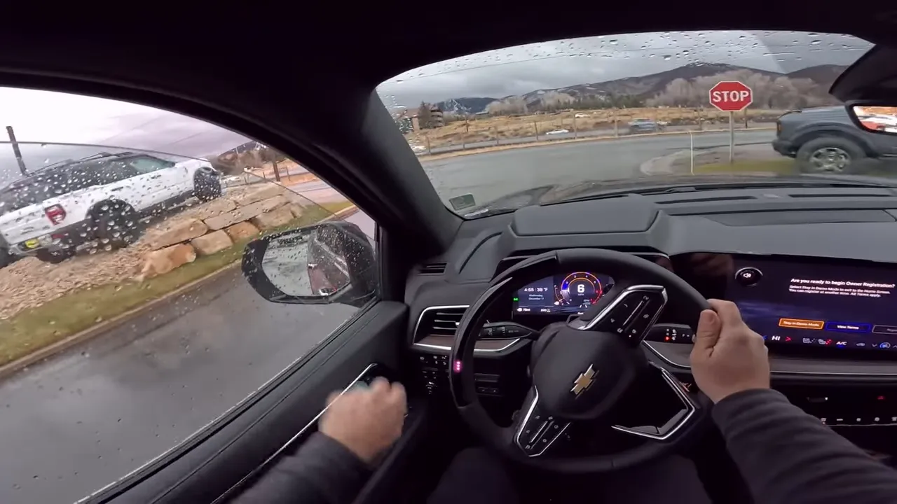 Driver view making a turn at a stop sign with raindrops on the windshield, steering wheel turned and parked trucks visible on the roadside