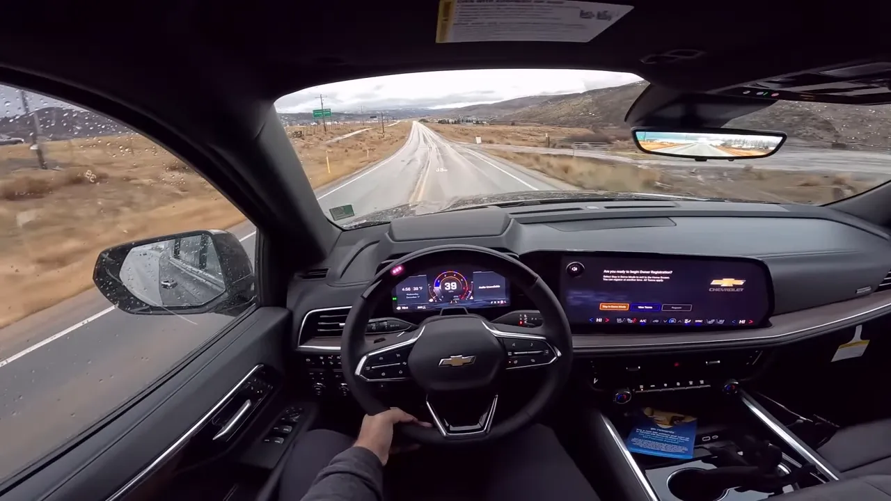 Driver-focused view inside a Chevrolet Suburban showing the digital instrument cluster, steering wheel and center infotainment screen with a clear view of the road ahead.