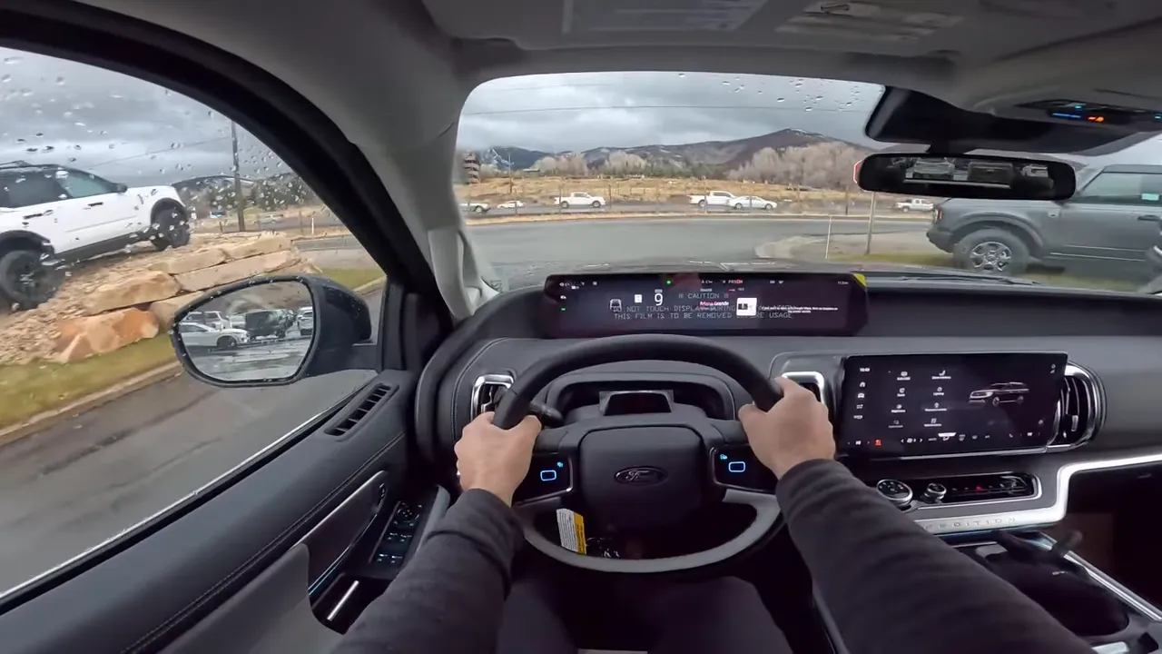 Straight-on driver view showing the non-circular Ford steering control with illuminated touch buttons, wide digital instrument display and center infotainment screen.