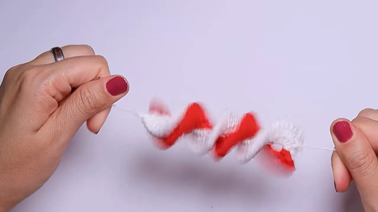 Hands holding a completed red-and-white crochet spiral stretched horizontally