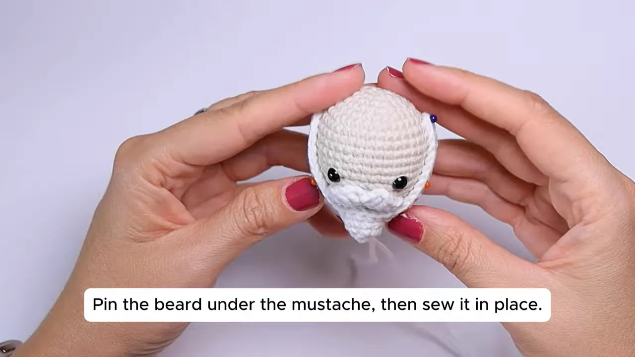 Crocheted Santa head with black eyes, white mustache, and pointed white beard pinned around the lower face