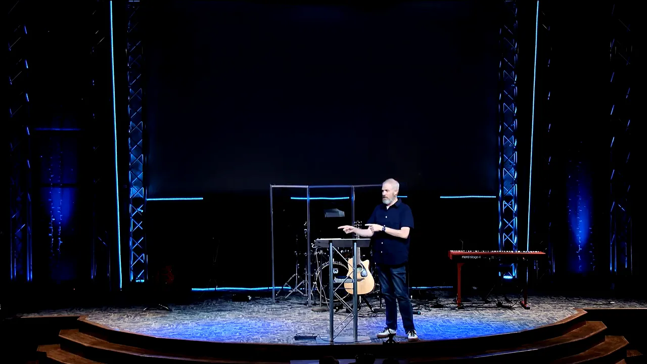Speaker presenting from behind a lectern on a church stage with instruments in the background