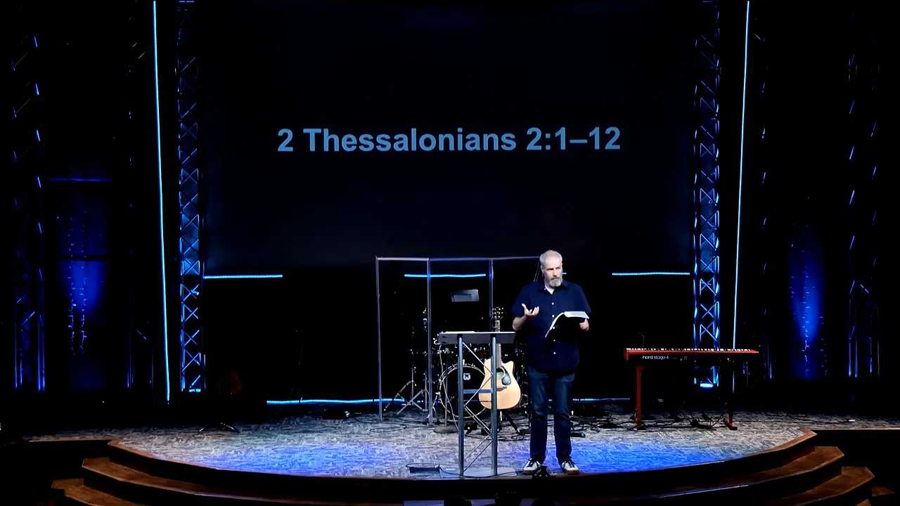 Pastor gesturing while teaching on stage with “2 Thessalonians 2:1–12” projected