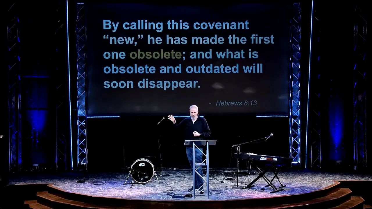 Wide shot of speaker on stage with a large slide reading 'By calling this covenant 